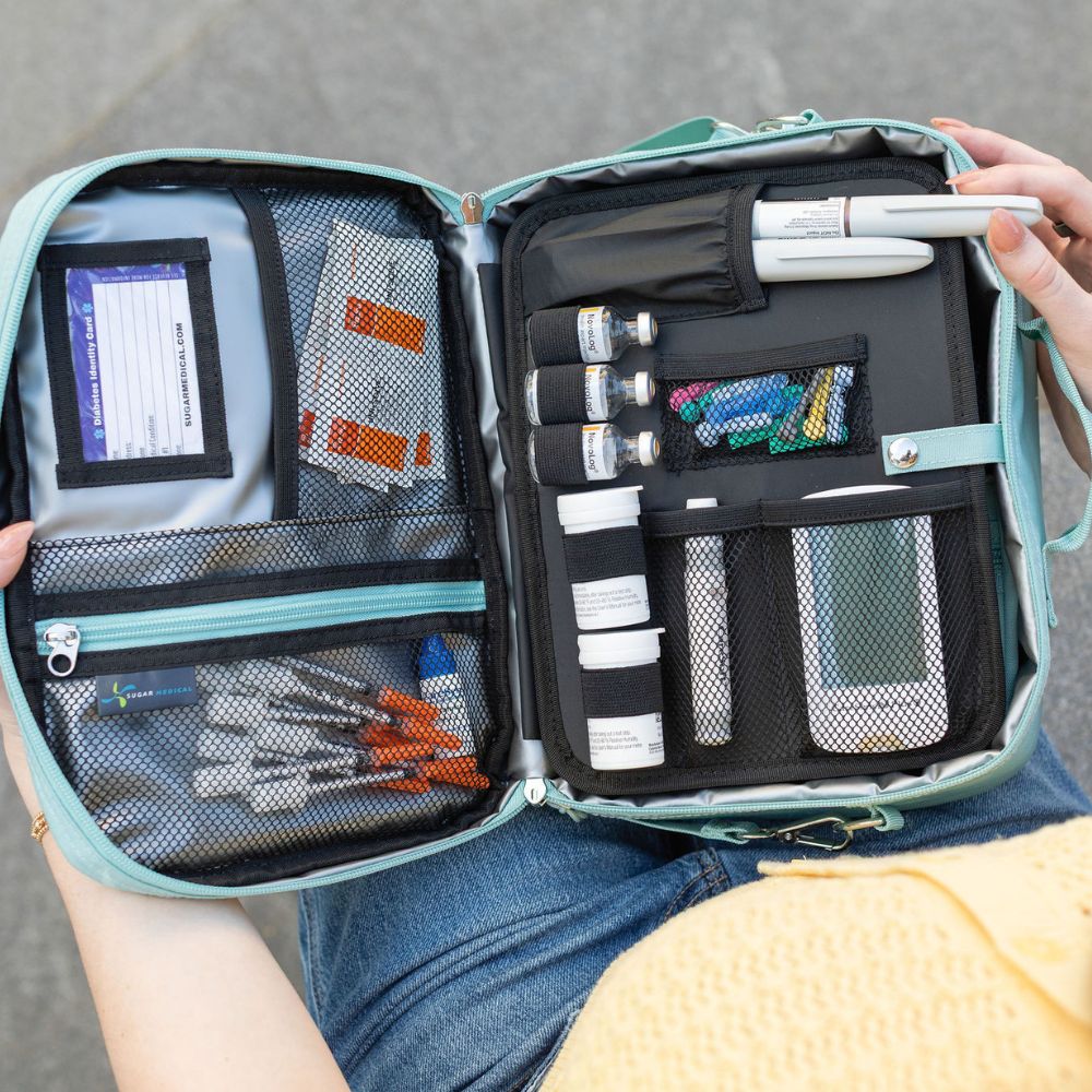 An open medical travel kit organizer held by a person, showing various medical supplies including vials, bandages, tweezers, and a name card.