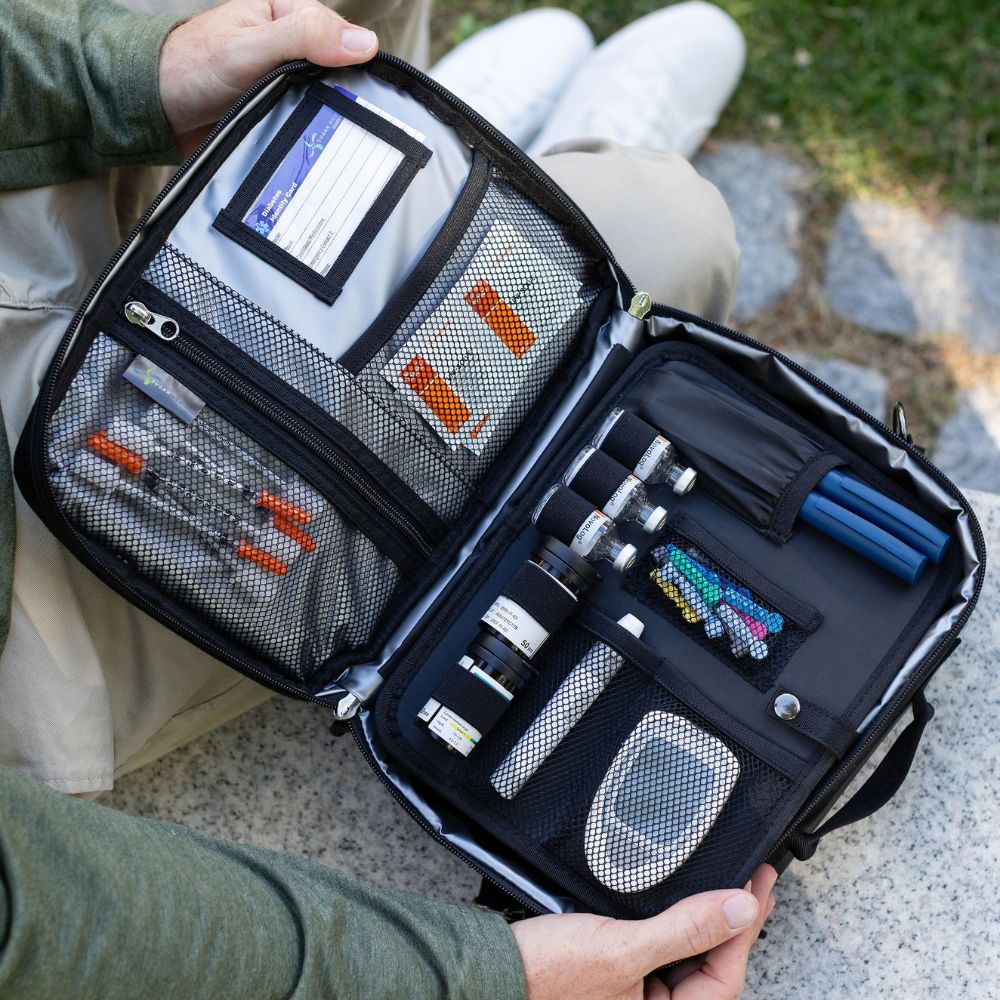Open travel diabetes bag with various items including organized diabetes supplies, held by a person outdoors.
