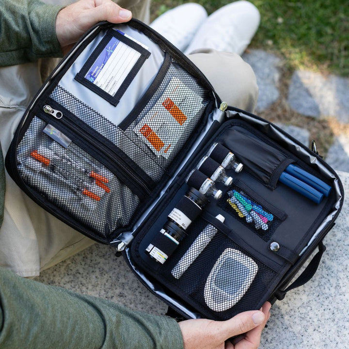 Open travel diabetes bag with various items including organized diabetes supplies, held by a person outdoors.