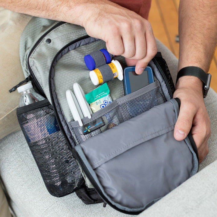 Diabetes Insulated Sling Backpack in grey opened with diabetic supplies organized in it on men’s lap. 