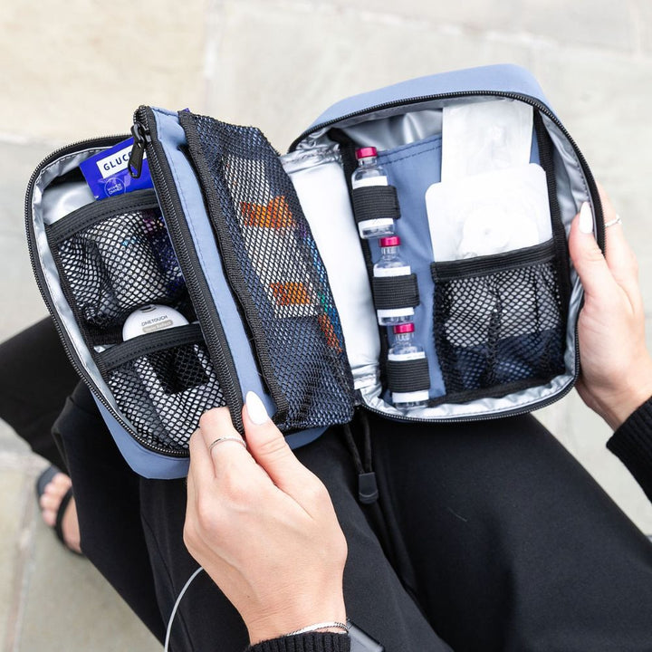 Woman holding open a Steel Blue Insulated Diabetes Organizer, displaying neatly arranged insulin and diabetes testing supplies.