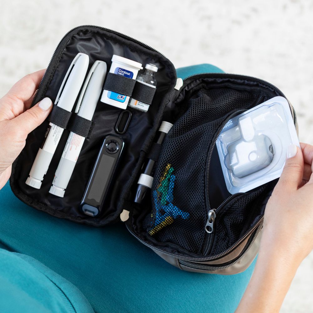 Diabetes Nylon Belt Bag inside set up with two insulin pens, glucose meter, test strips, insulin vial and mesh pocket to fit more diabetic supplies opened on a women’s lap.  