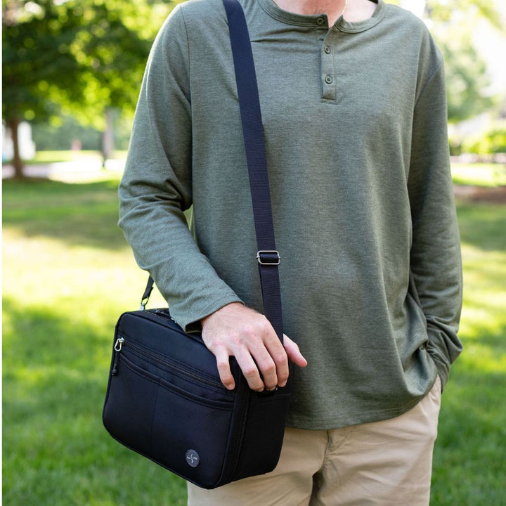Person holding a black diabetes travel bag outdoors with greenery in the background