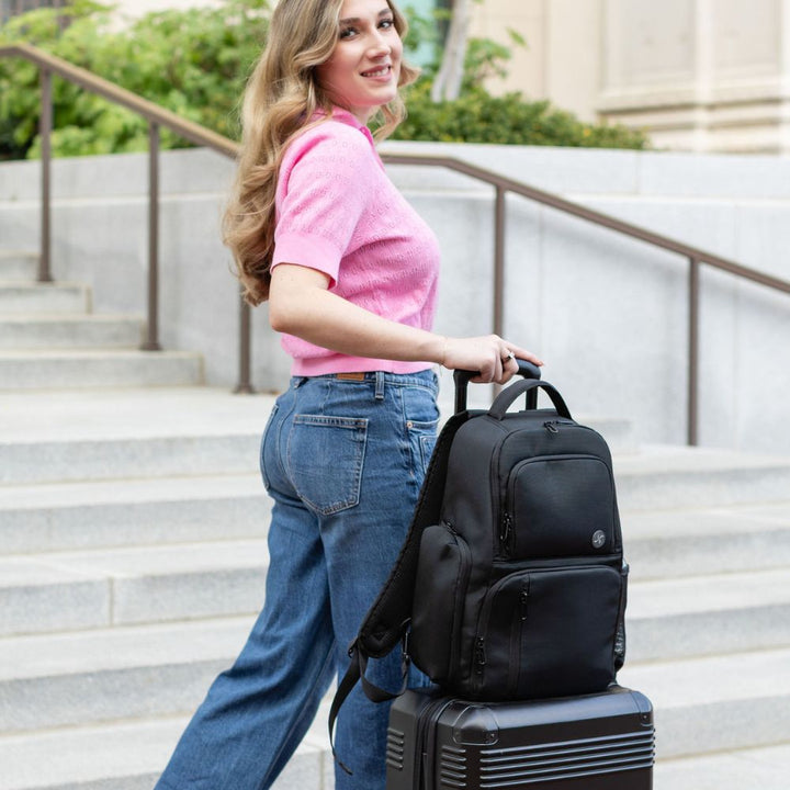 Woman holding a black backpack and suitcase on steps outdoors