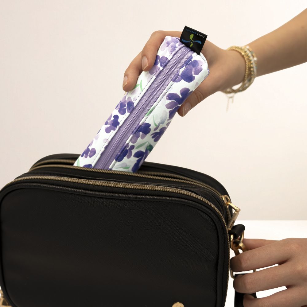 Hand holding a floral-patterned MedMate over a black bag with a beige background
