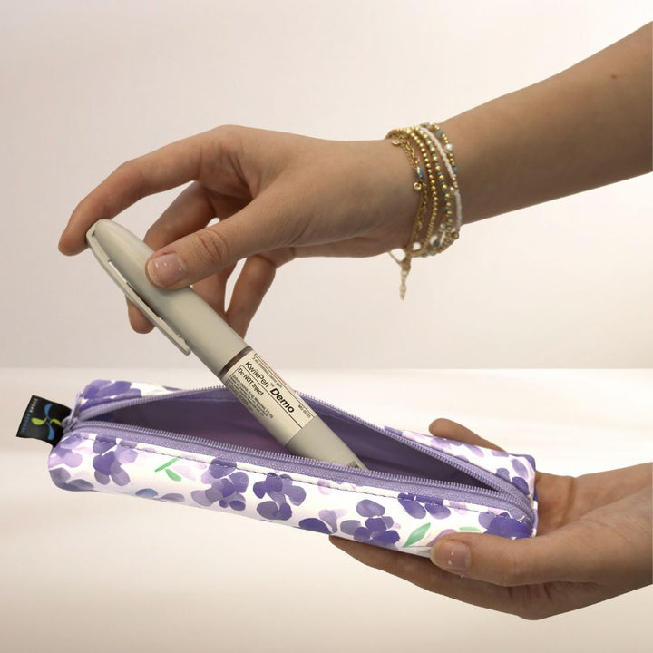 Hand holding a insulin pen over a floral Medmate with a white background