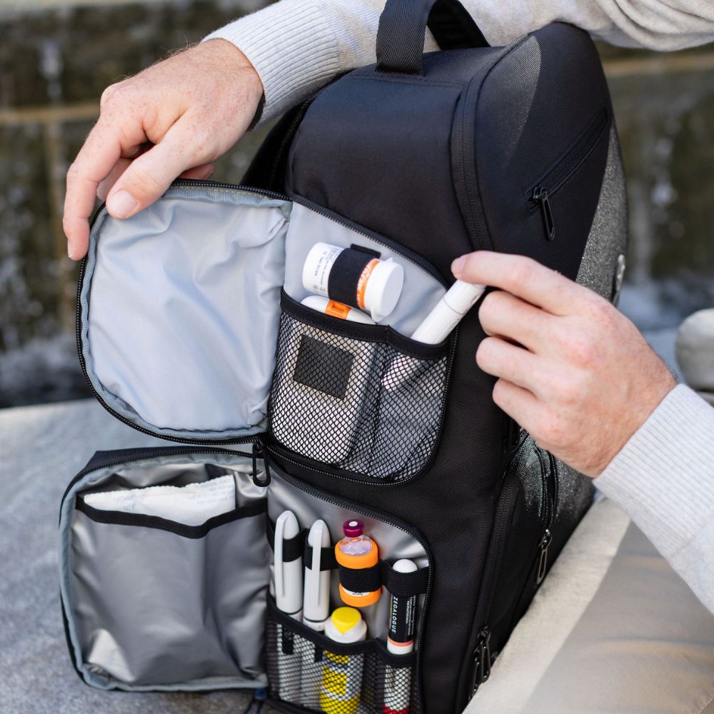 Person opening a black backpack with compartments containing diabetes supplies.