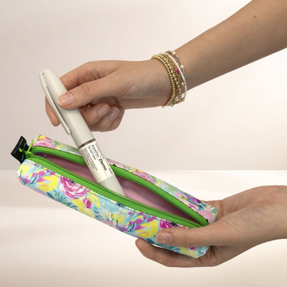 Hand holding a floral MedMate with a pen inside against a plain background