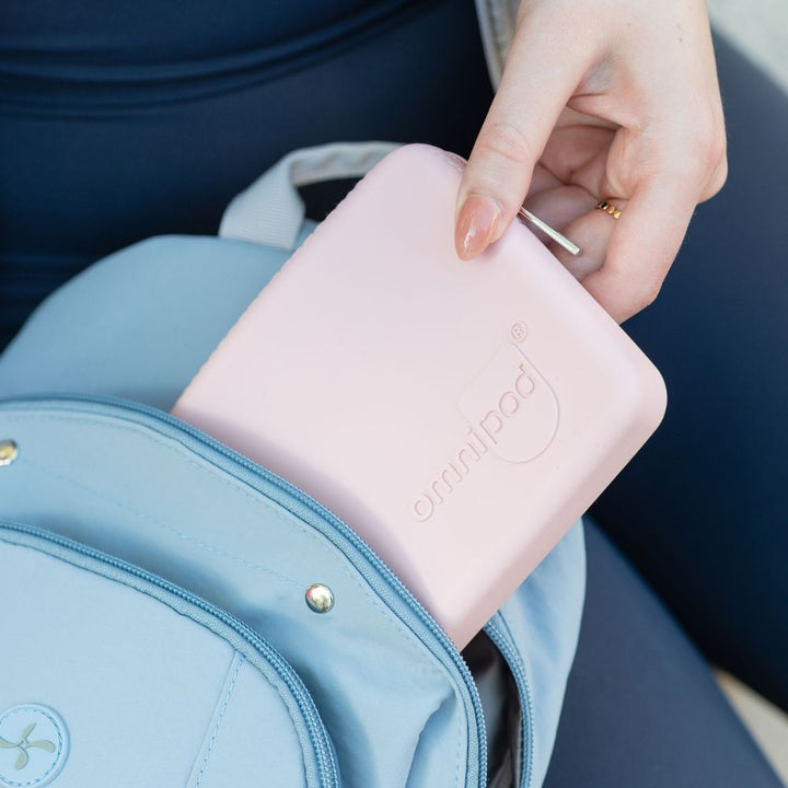 Person placing a pink Omnipod Trave Casei nto a blue sling backpack.