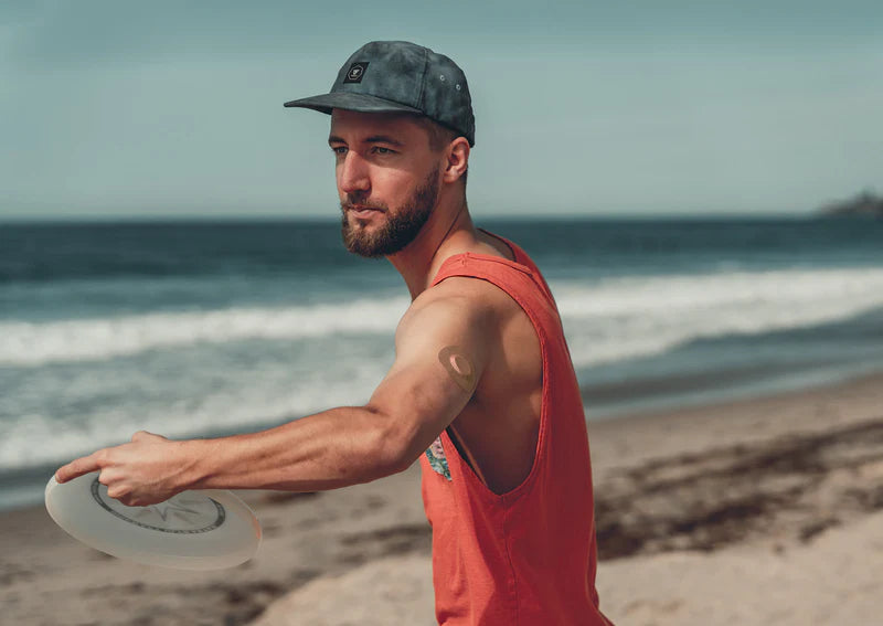 Dexcom G7 sensor covered with a tan Skin Grip patch on a man's upper arm while he throws a frisbee—illustrating secure, active wear and freedom of movement during outdoor activity.