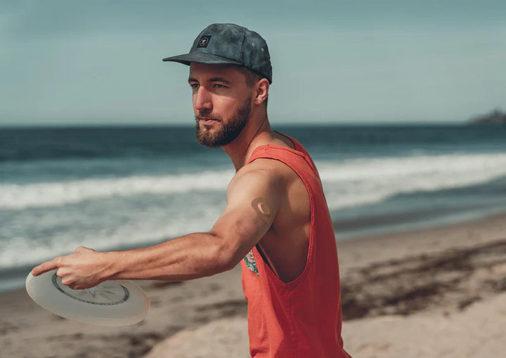 Dexcom G7 sensor covered with a tan Skin Grip patch on a man's upper arm while he throws a frisbee—illustrating secure, active wear and freedom of movement during outdoor activity.