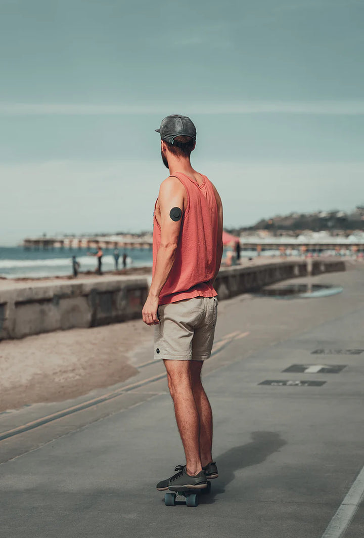 Dexcom G7 sensor covered with a black Skin Grip patch on a man's upper arm while he rides skateboard—illustrating secure, active wear and freedom of movement during outdoor activity.