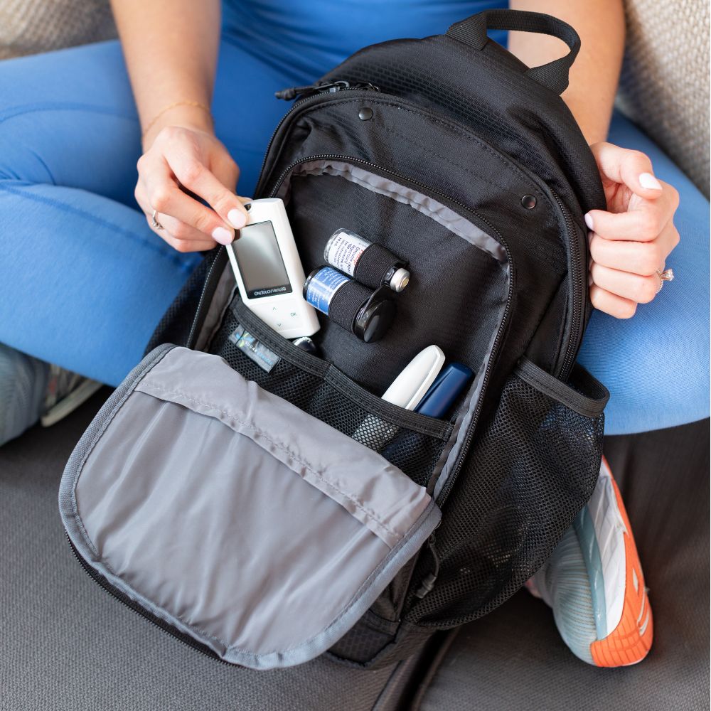 Diabetes Insulated Sling Backpack in black opened with diabetic supplies organized in it on women’s lap. 