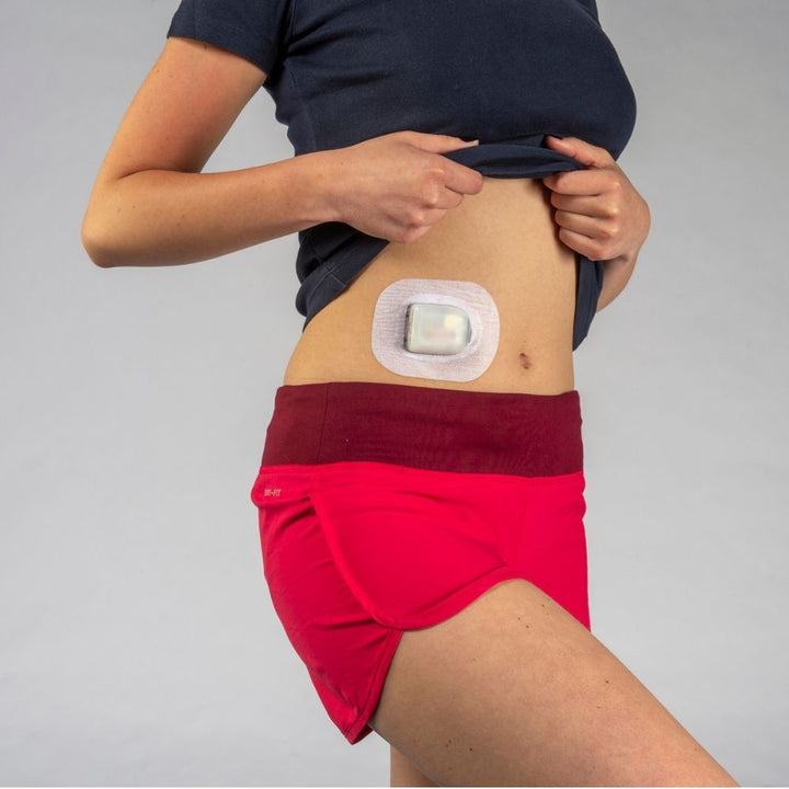 A woman in red shorts and a black shirt wearing the pod and Podpal on the right side of her stomach.