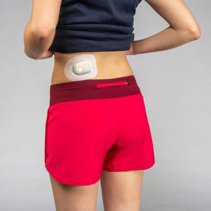 A woman in red shorts and a black shirt wearing the pod and Podpal on the left side of her lower back.