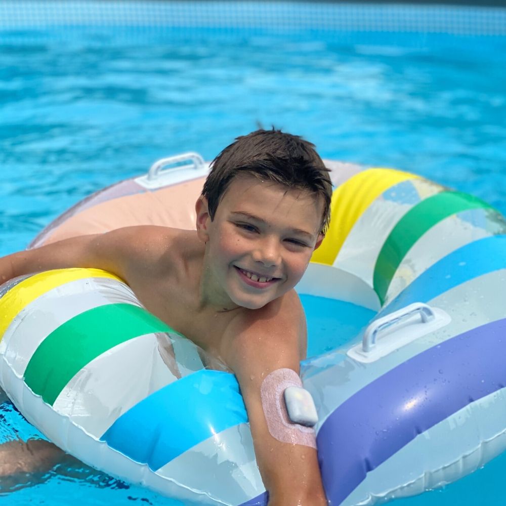 A young boy in a pool swimming in a round float wearing the pod and Podpal on the upper section of his left arm.